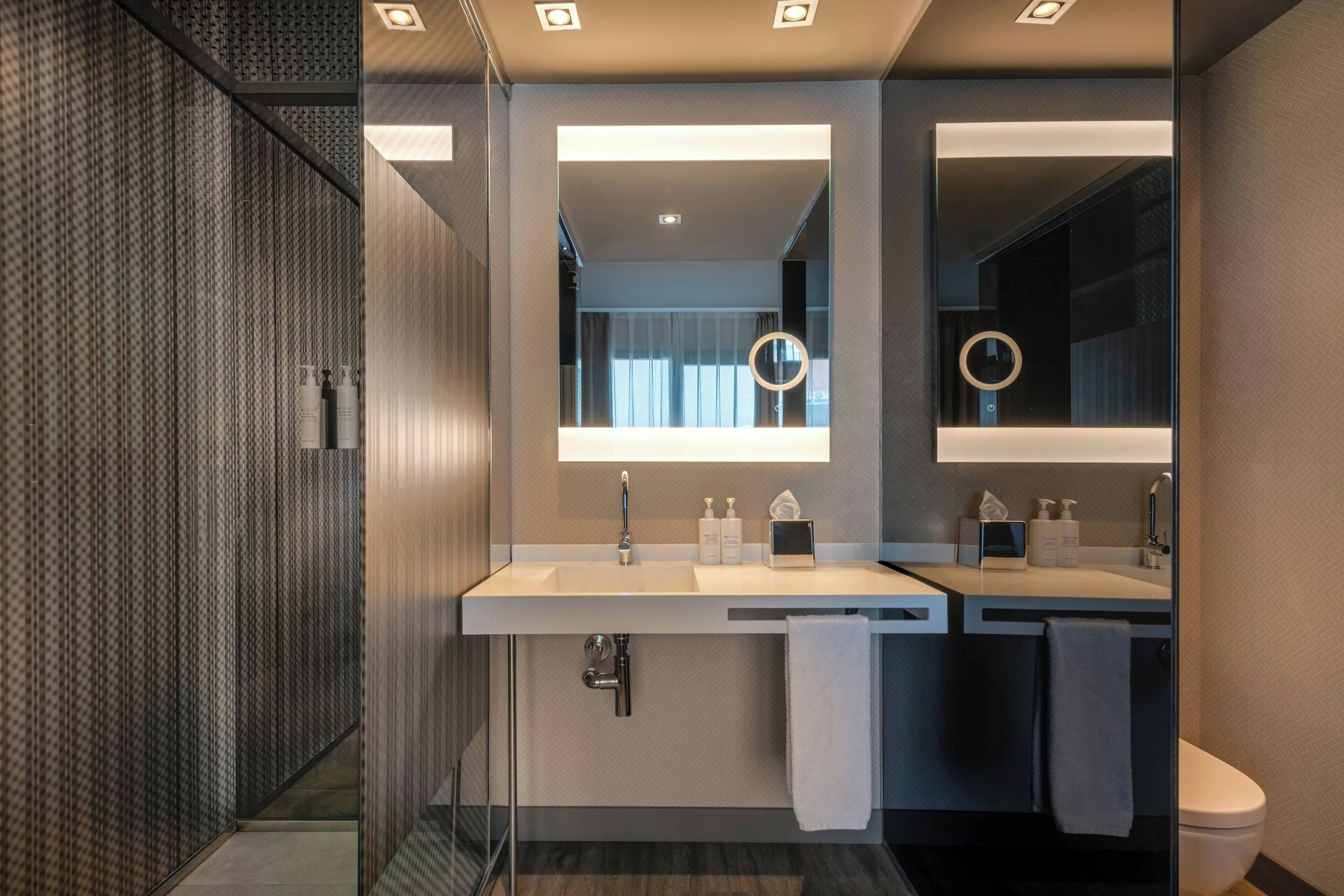 Un baño moderno con cabina de ducha de vidrio, dos lavamanos con espejos y un inodoro.