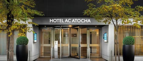 The entrance to HOTEL AC ATTOCHA with a glass door entrance and a sign above.