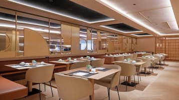 Un espace de restauration moderne dans un hôtel, avec de longues tables, des chaises confortables et un mur réfléchissant.