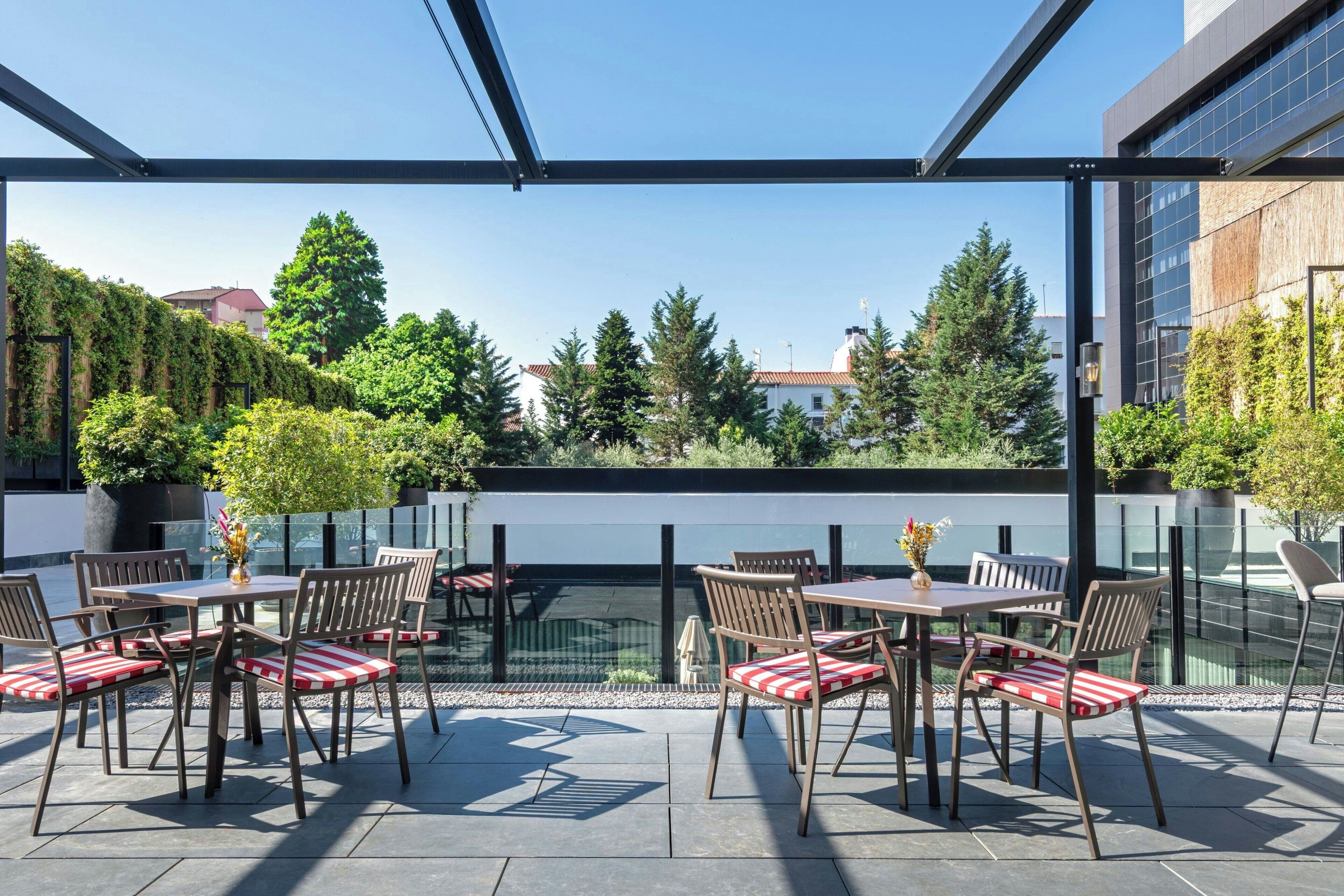 An outdoor patio area with tables and chairs, surrounded by glass walls and a view of trees and buildings.