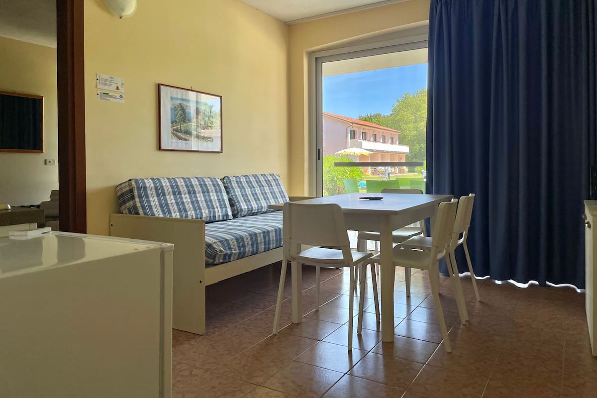 A room with a sofa, a dining table with chairs, a window with a view of buildings, and a door.