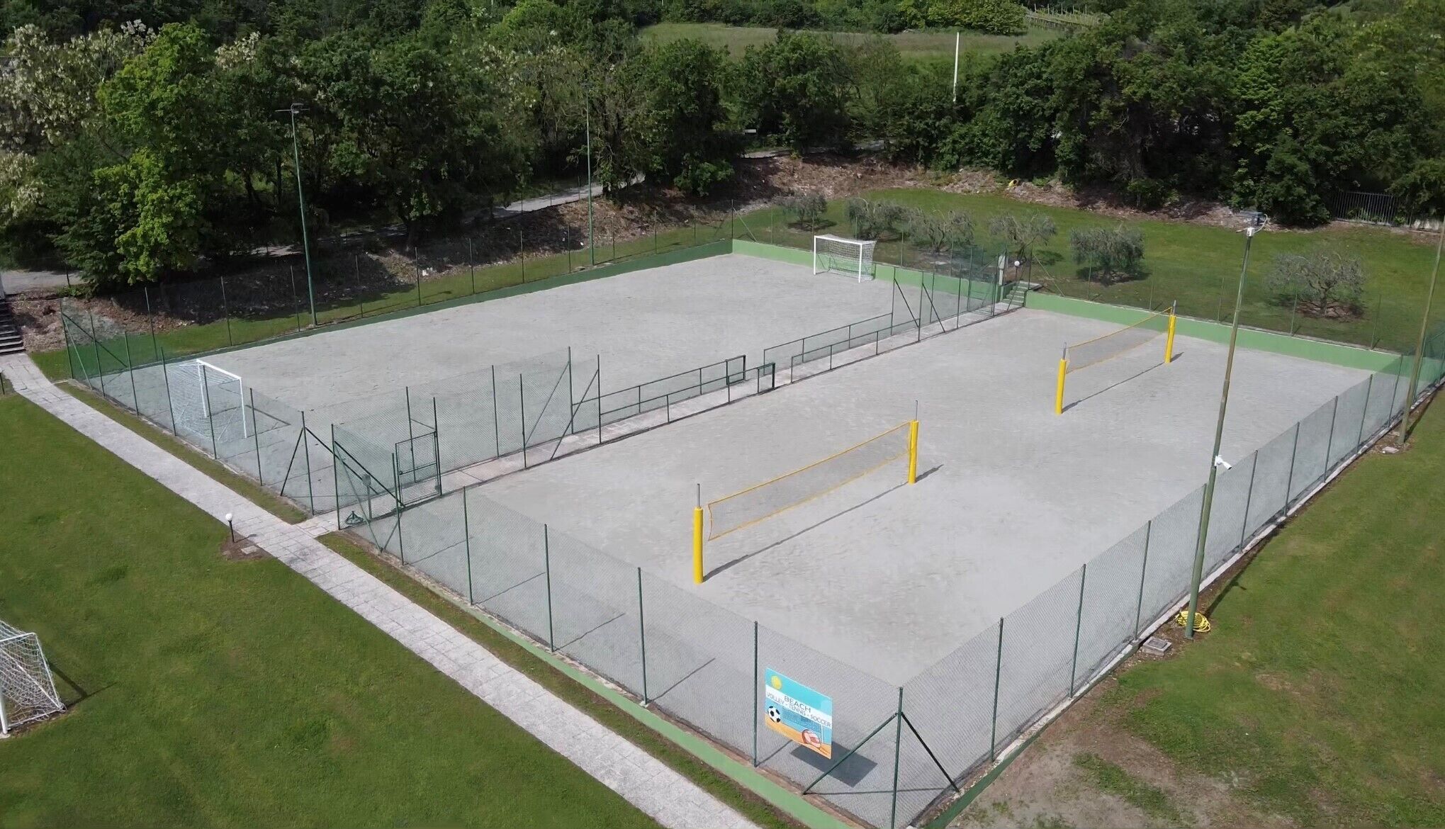 Een lege sportplek met een voetbaldoel, omringd door een hek en begroeiing.