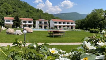 Experience serene tranquility amidst lush greenery and blooming flowers, surrounded by three charming buildings and a picturesque mountain backdrop.