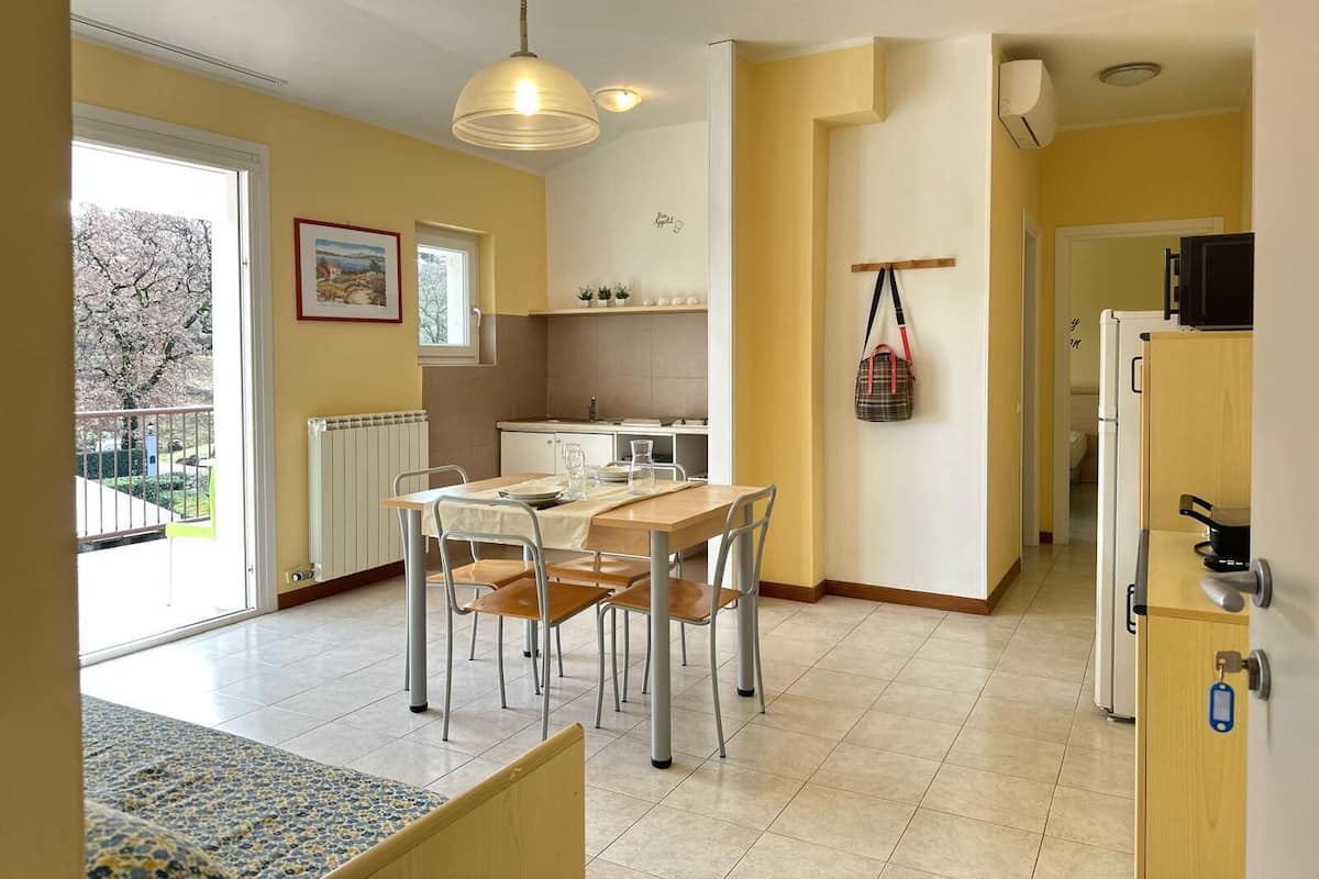 A bright kitchen with a dining area, a radiator, a hanging bag, and a view of the outside.