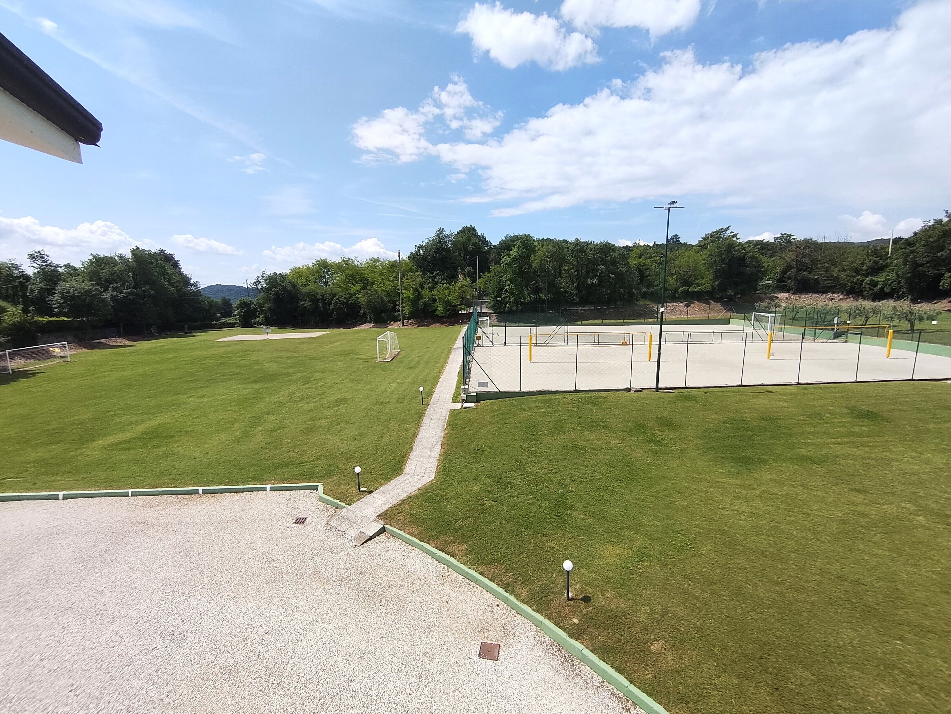 Un campo deportivo con un arco, una zona de grava y una valla verde.