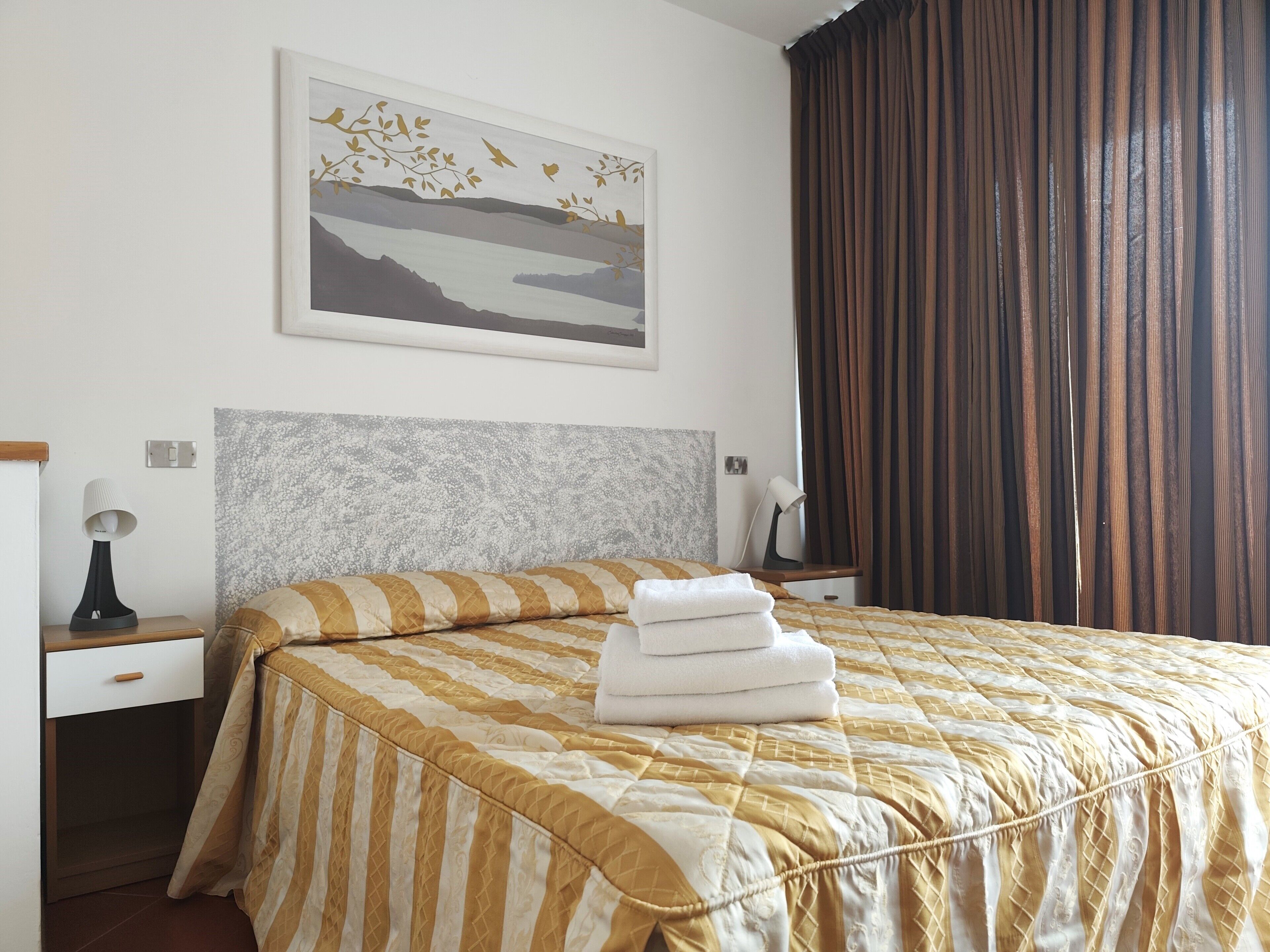 A hotel room with a bed, a nightstand, a lamp, a mirror, and a painting on the wall.