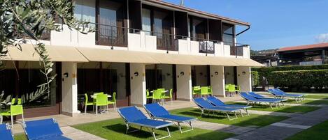 A hotel with a two-story structure, outdoor seating area with green chairs, and blue sun loungers.