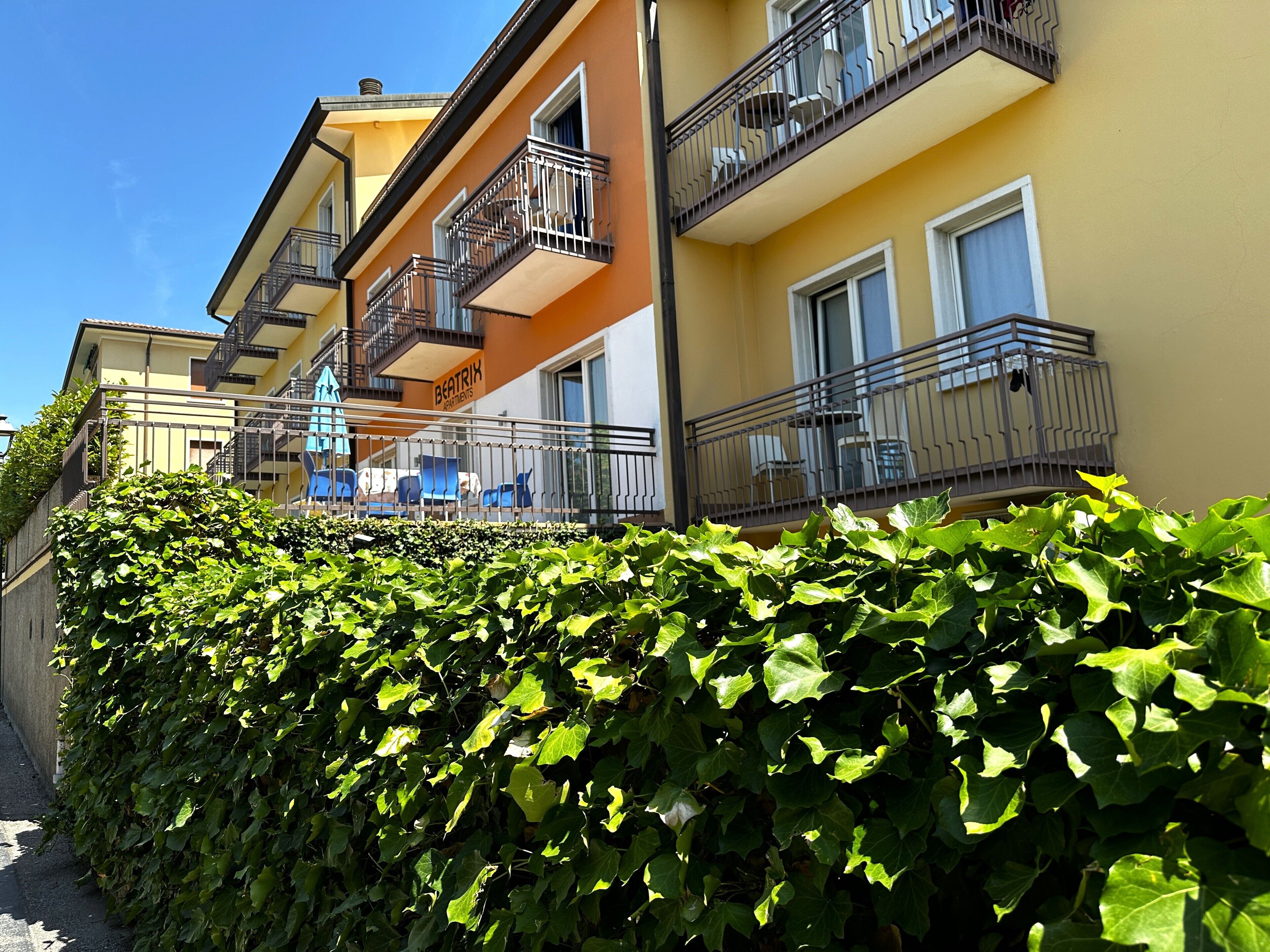 Un immeuble à plusieurs étages doté de balcons, un arbuste au premier plan et un ciel bleu dégagé.