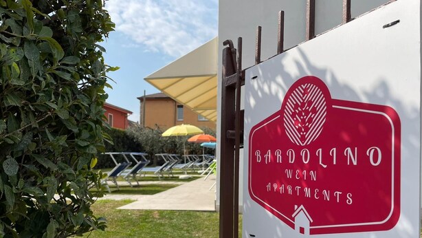 Skilt for Bardolino Weingroß Apartments med logo og tekst, der angiver at det er et lejlighedskompleks.