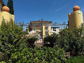 A multi-story building with balconies, a gated entrance, and surrounding greenery. - Beatrix - Apartments (Bardolino)