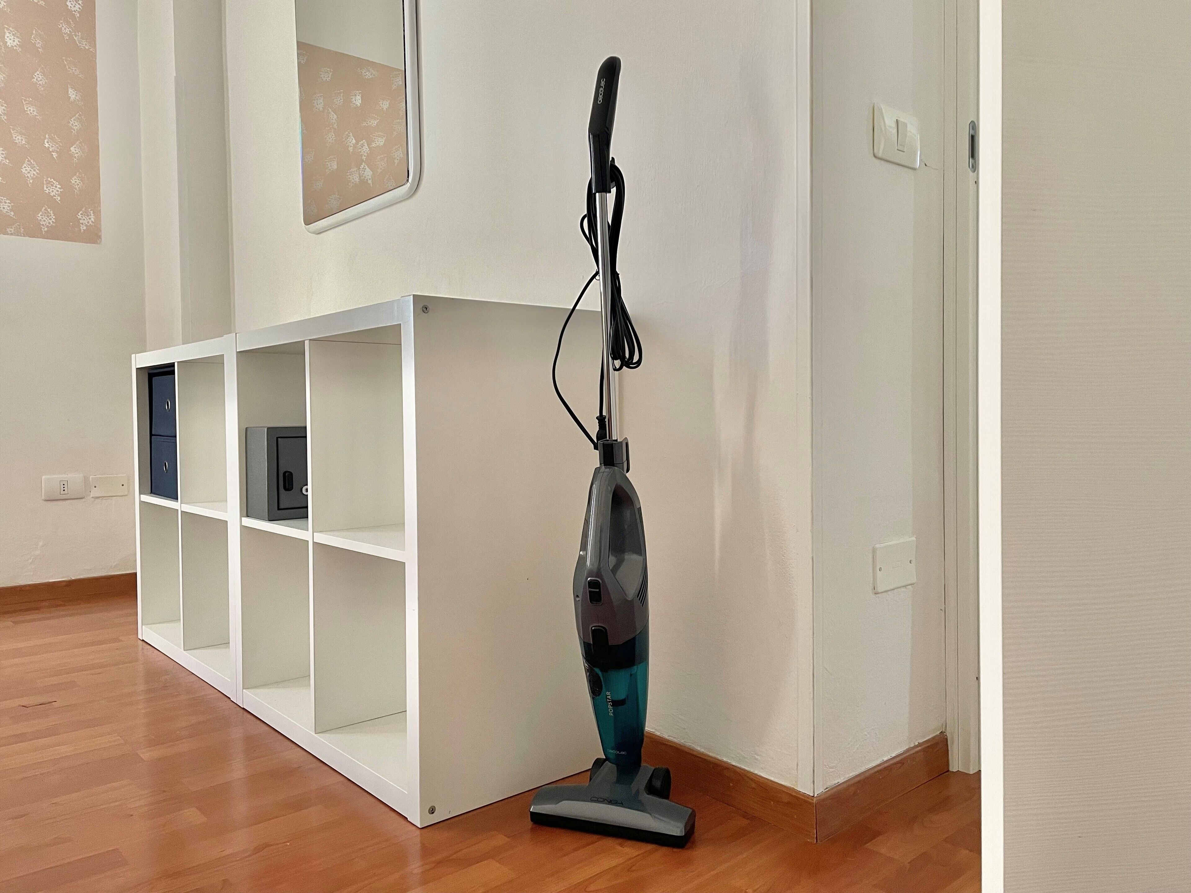 A room with a white shelving unit, a vacuum cleaner, and a wooden floor.