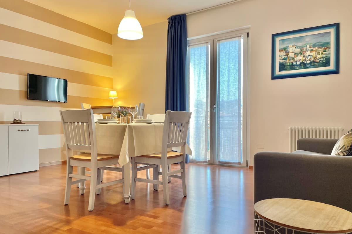 Un comedor con una mesa lista para cuatro personas, un sofá, un radiador y un cuadro en la pared.
