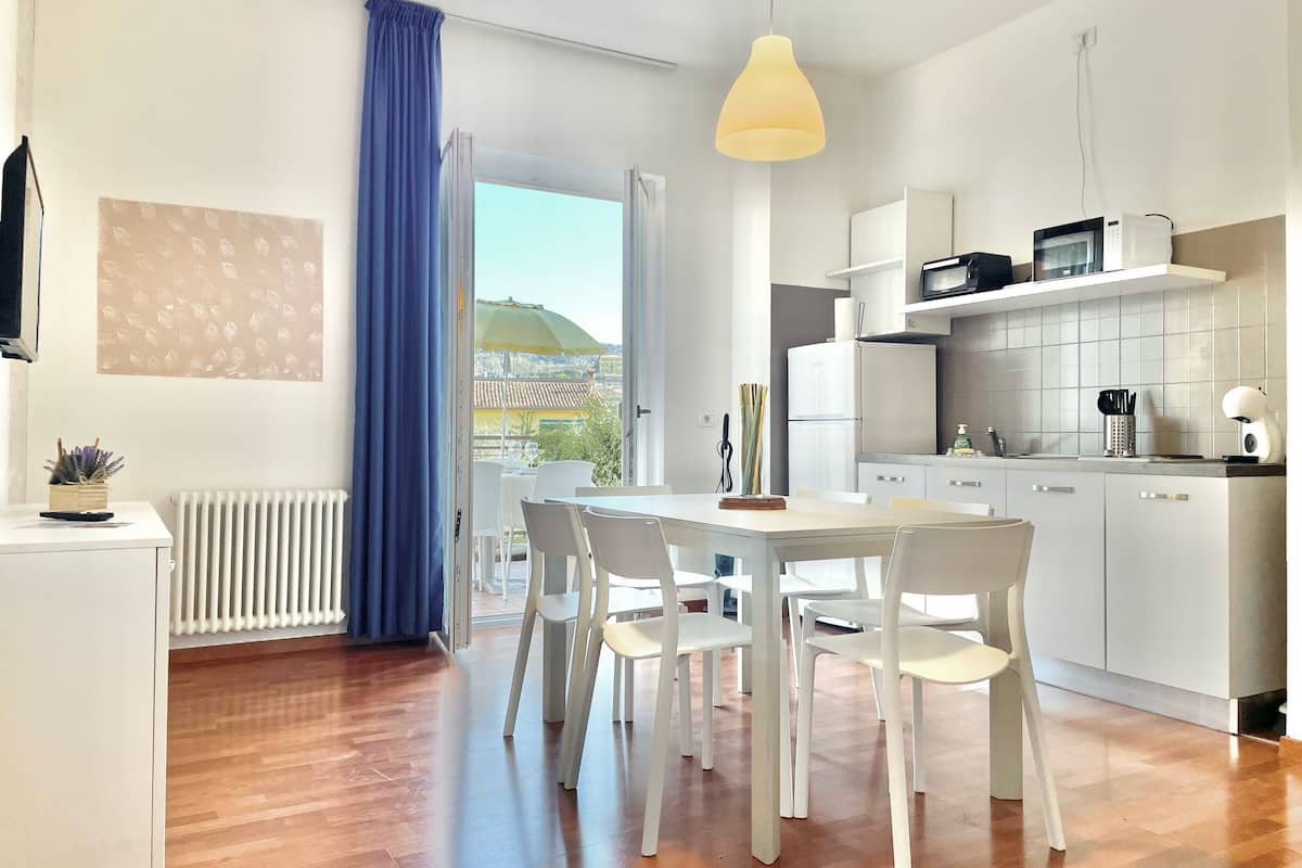 Una cocina moderna con armarios blancos, un microondas y un comedor con mesa y sillas.