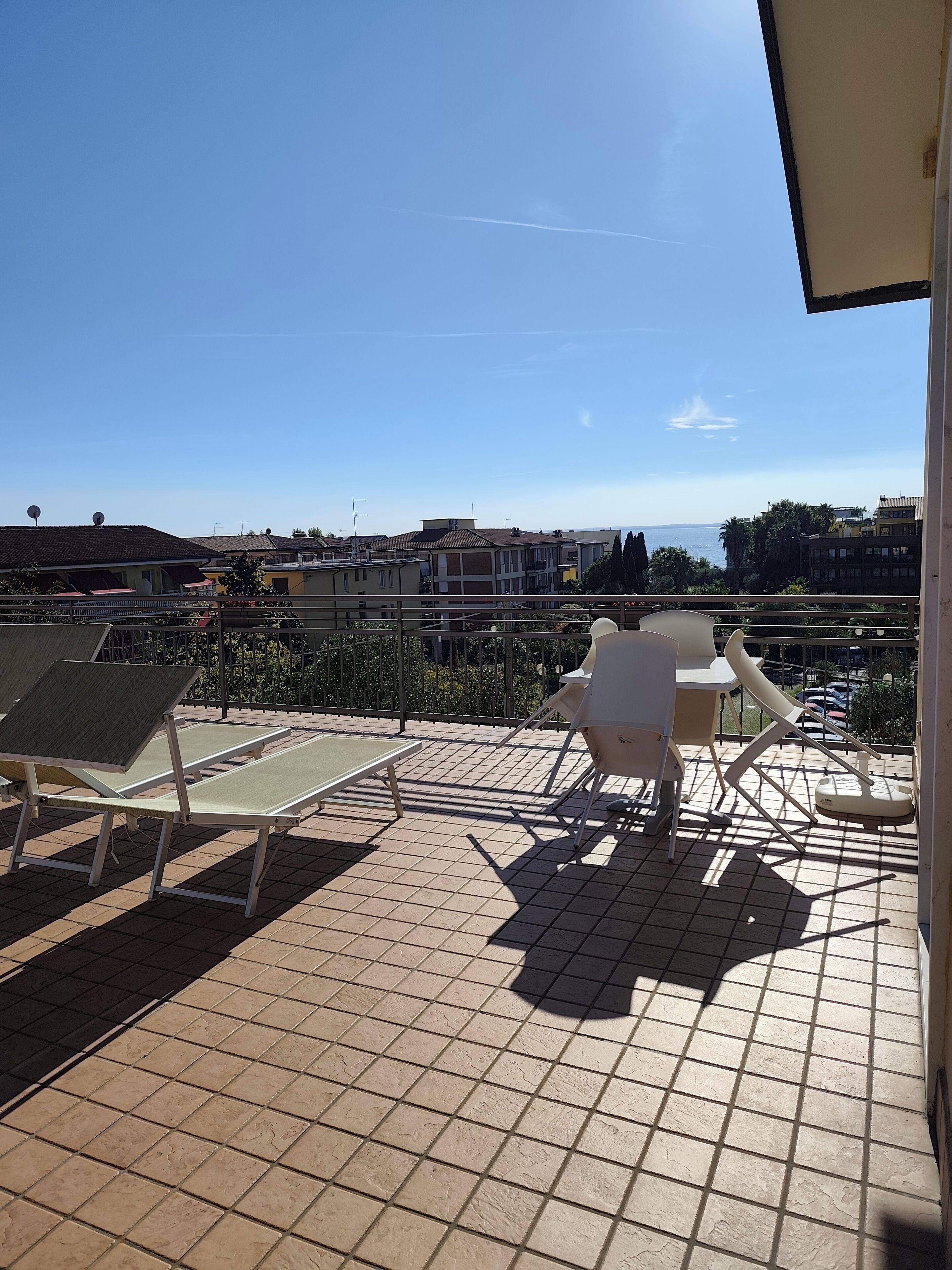 A balcony with two sun loungers and a table, overlooking a residential area with buildings and a body of water.