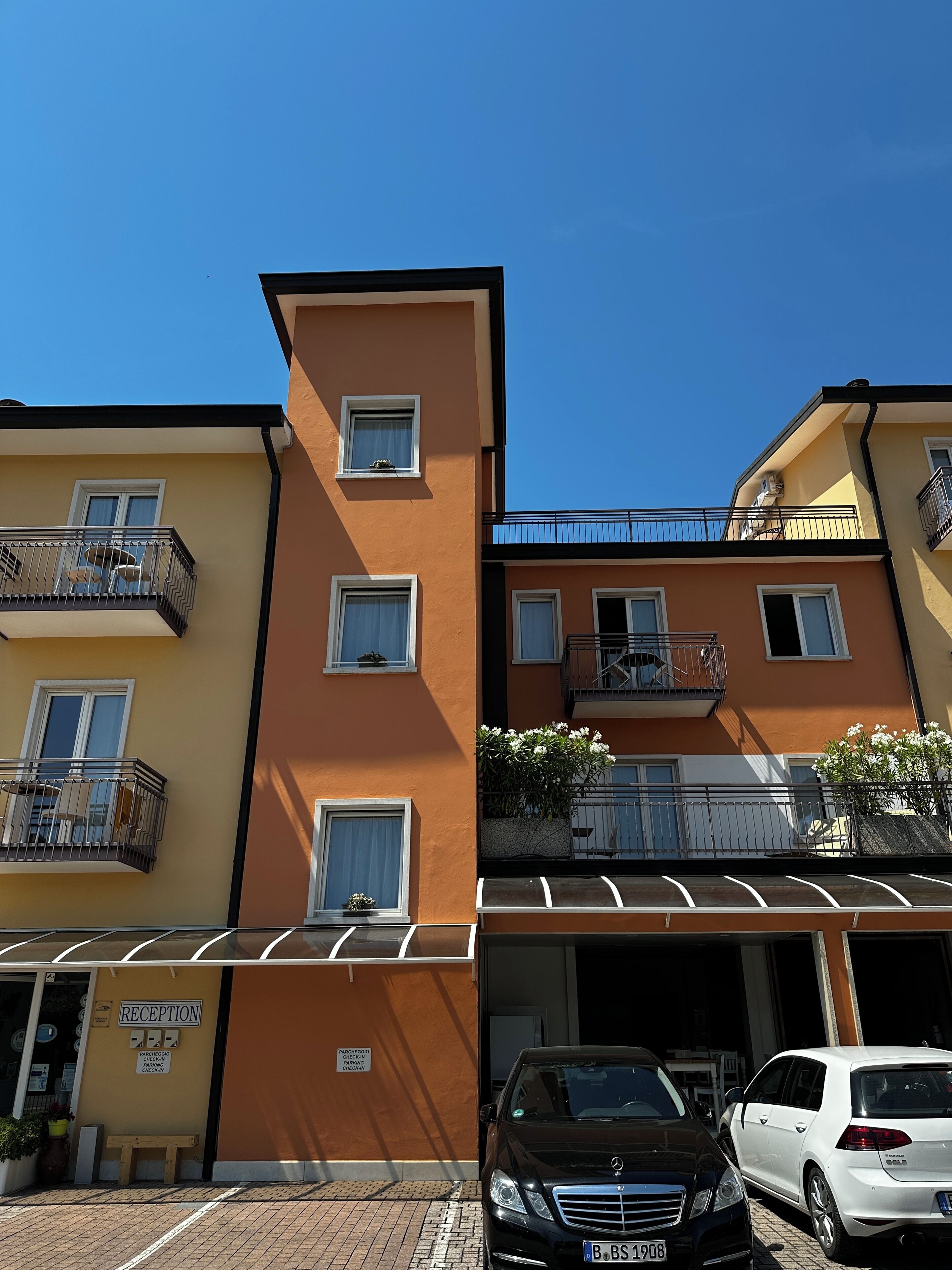 Un edificio de varios pisos con balcones, una recepción y un estacionamiento.