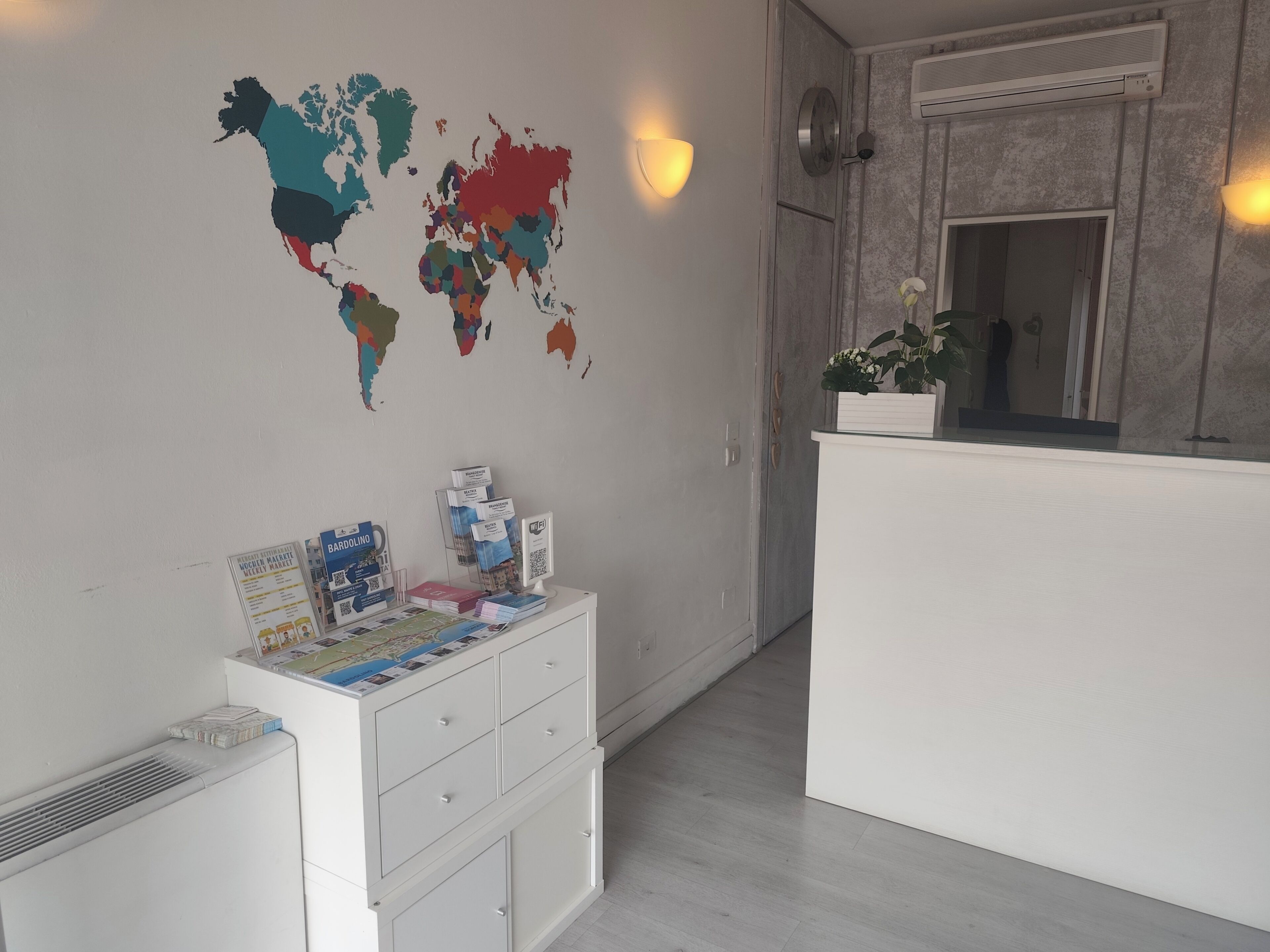 A reception area with a world map, a white desk with brochures, a white cabinet, and a wall-mounted air conditioner.