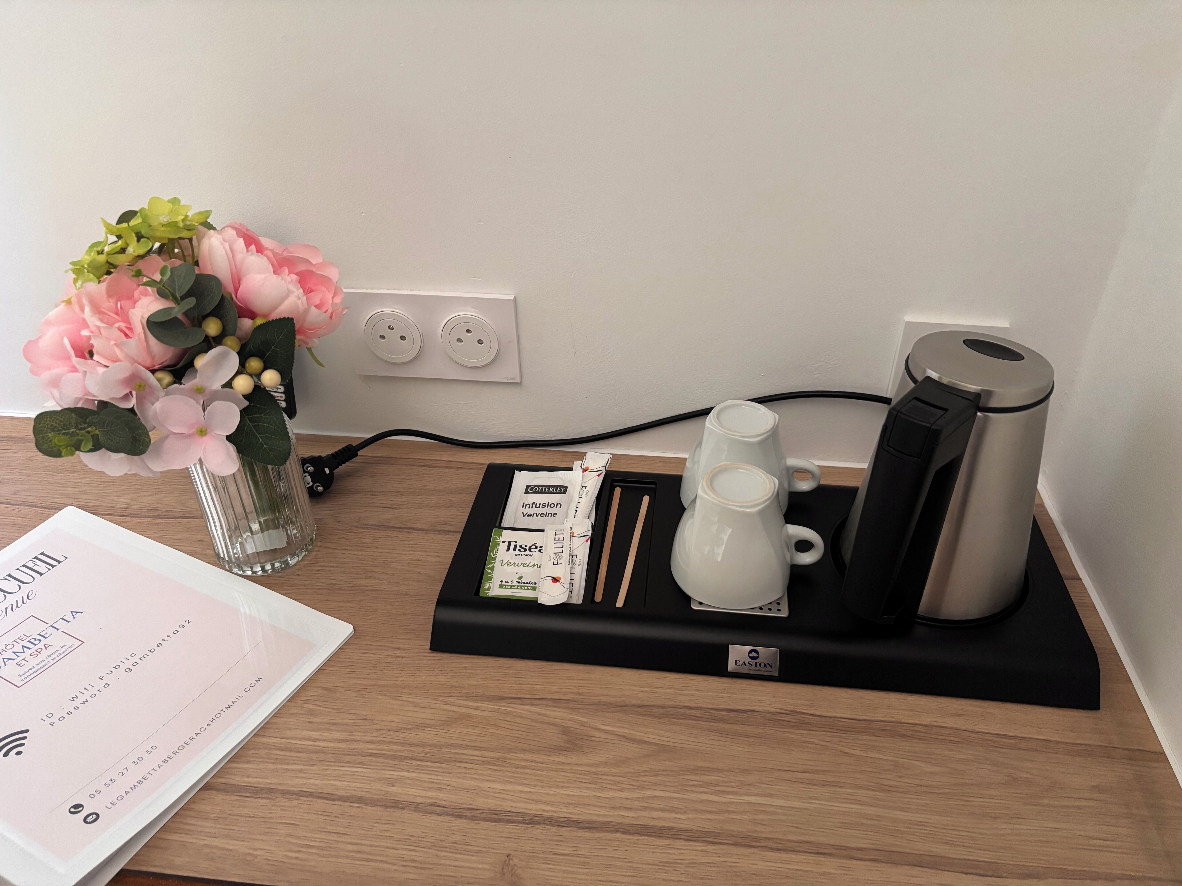 Une chambre d’hôtel avec un bureau en bois, un vase de fleurs, une machine à café et une station de recharge.