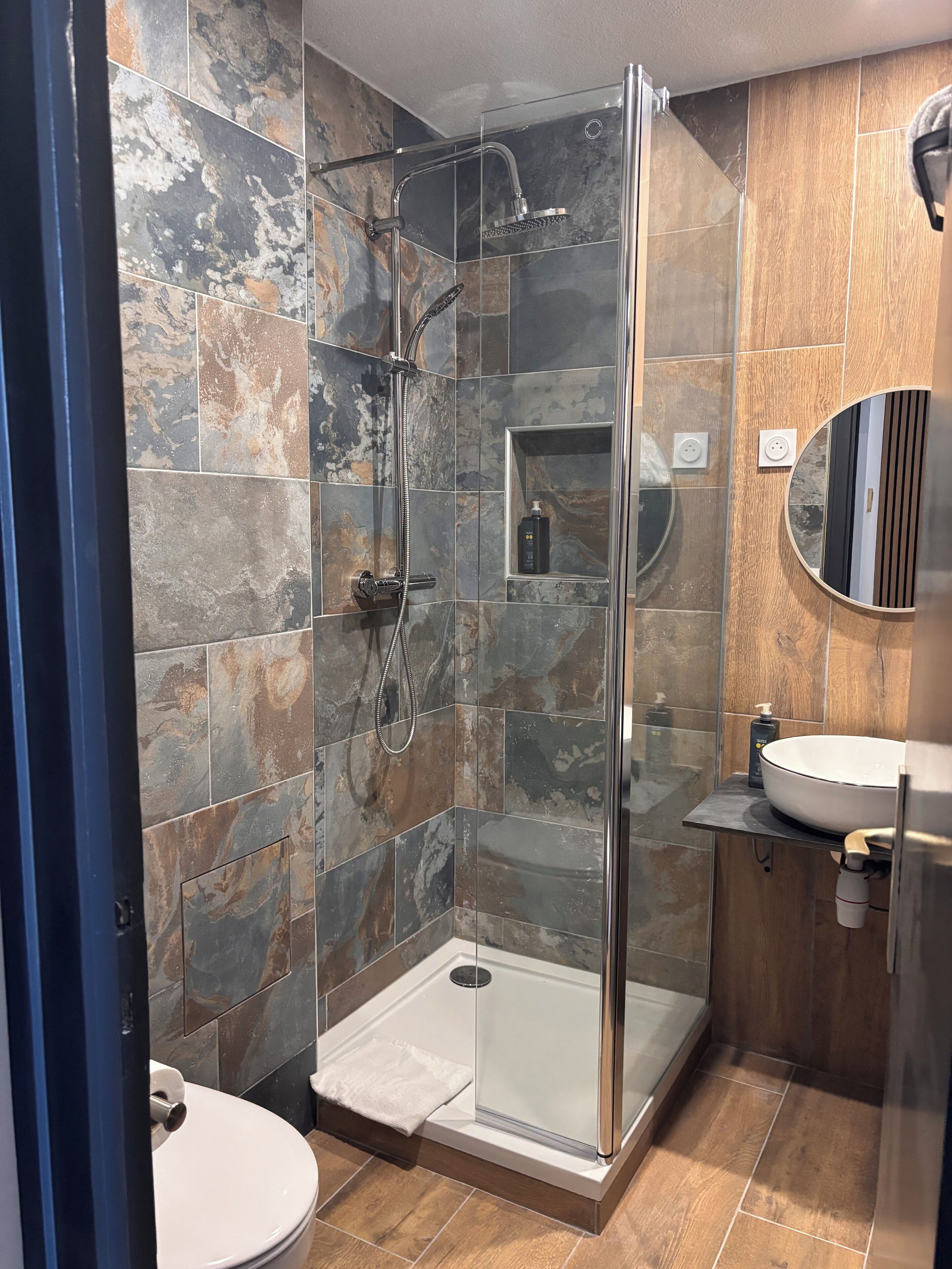 A modern bathroom with a glass-enclosed shower, a white sink, and a marble-tiled wall.