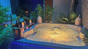 A hot tub surrounded by plants and candles, with a wooden structure in the background. - Hôtel & SPA Le Gambetta, Centre-ville, Bergerac (Bergerac)