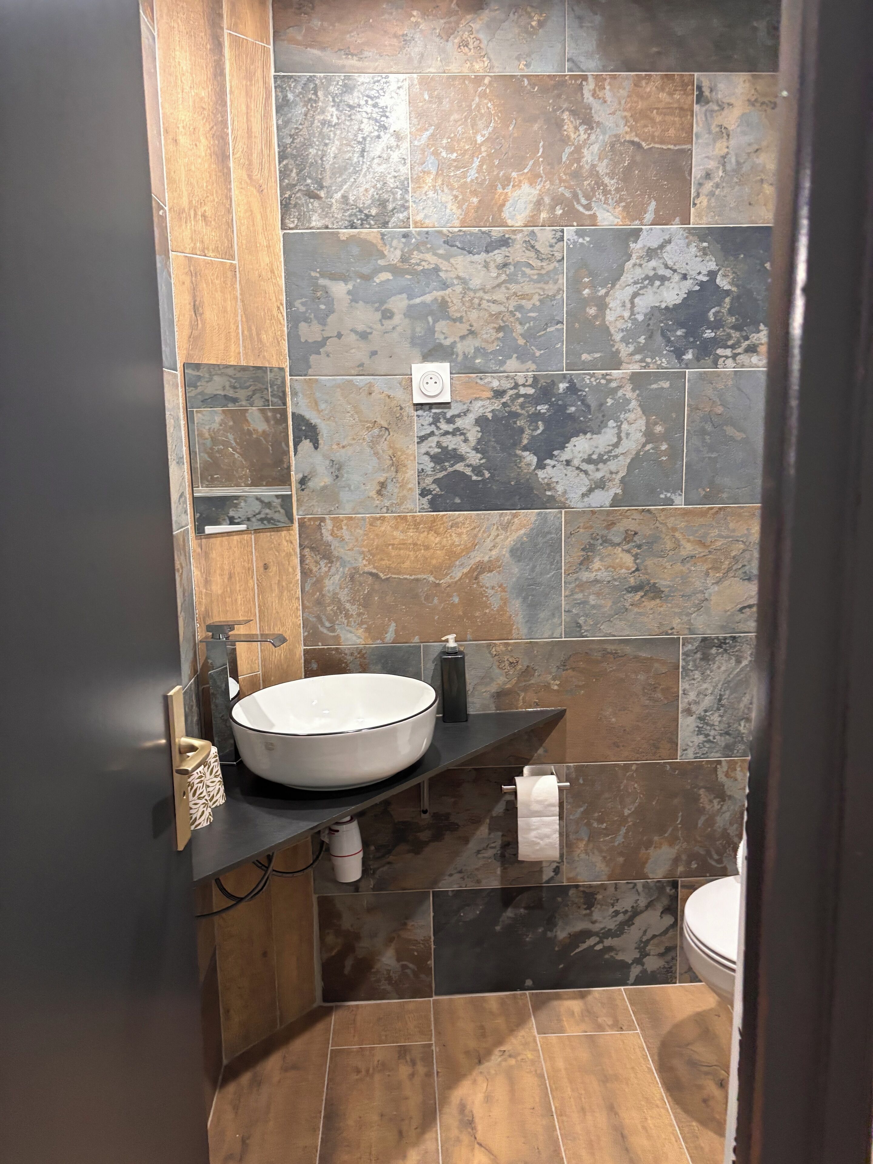 A bathroom with a large white sink, dark tiles, and a wooden accent wall.