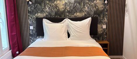 A bedroom with a large bed, a tropical wallpaper, a red curtain, and a wooden floor.