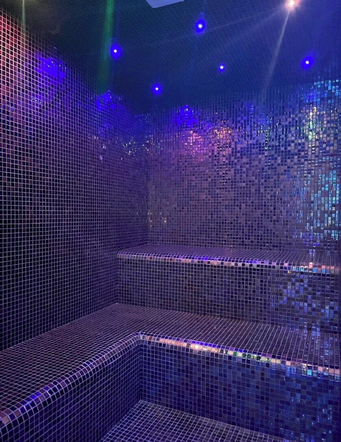 A tiled room with a seating area and a wall with a reflective surface.