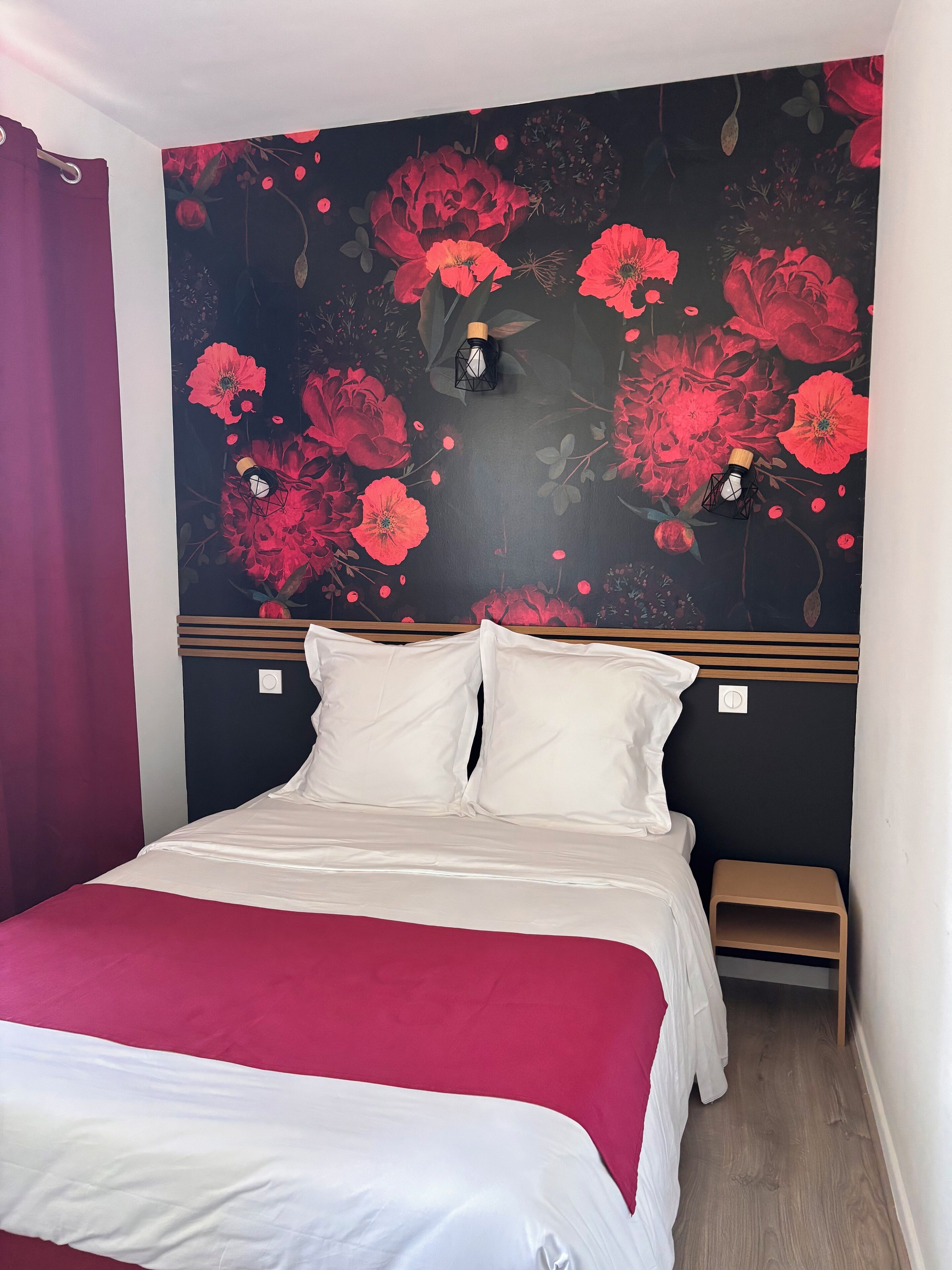 A bedroom with a bed, pillows, a bedside table, and a wall with a floral mural.