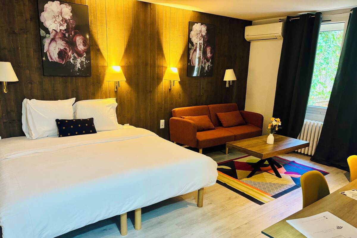 A hotel room with a large bed, a sofa, a small table, and a window with curtains.