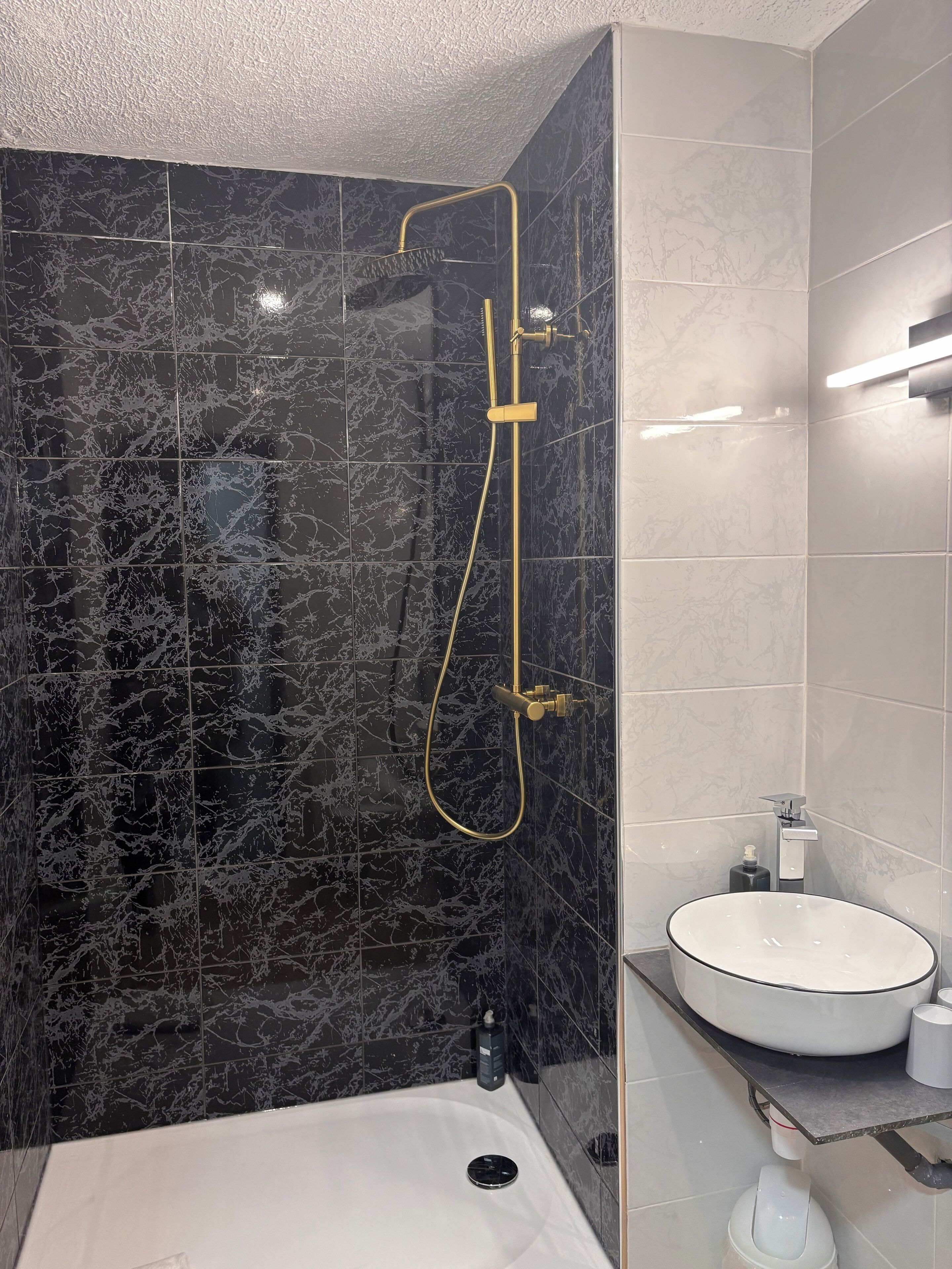 Une salle de bain avec un mur en marbre noir, une pomme de douche dorée, un lavabo blanc et des toilettes.