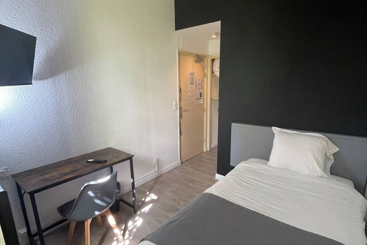 A modern hotel room with a bed, a desk, and a chair. There is a flat-screen TV mounted on the wall.