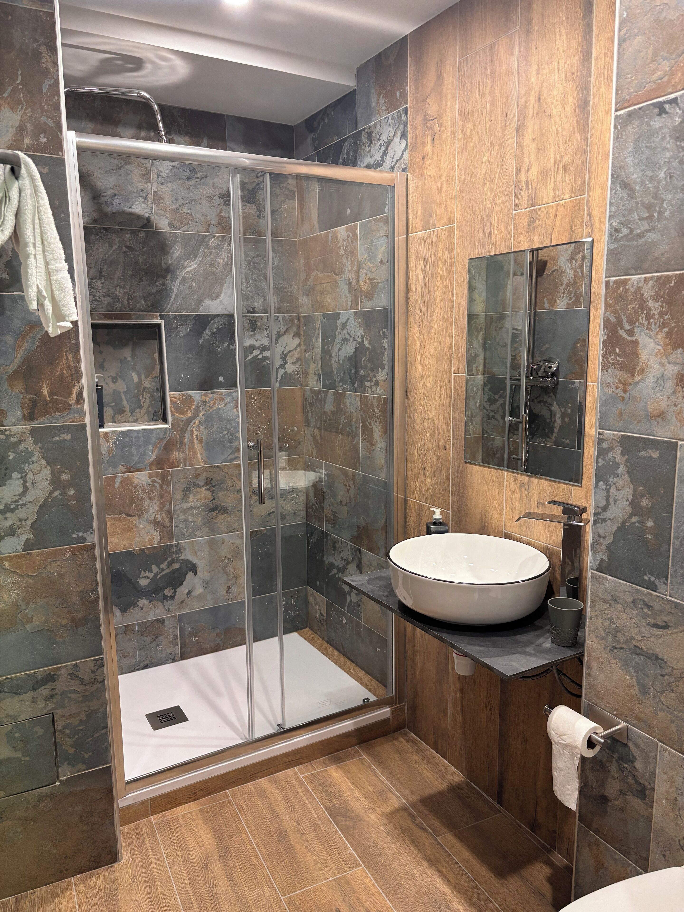 A modern bathroom with a glass-enclosed shower, a large white sink, and a wooden vanity.