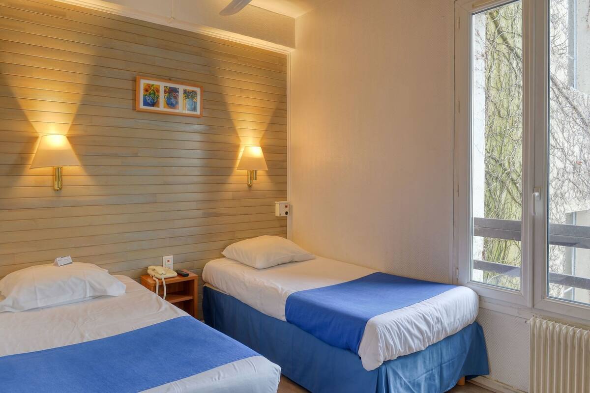 A hotel room with two beds, a wooden wall, a window, and a nightstand with a phone.