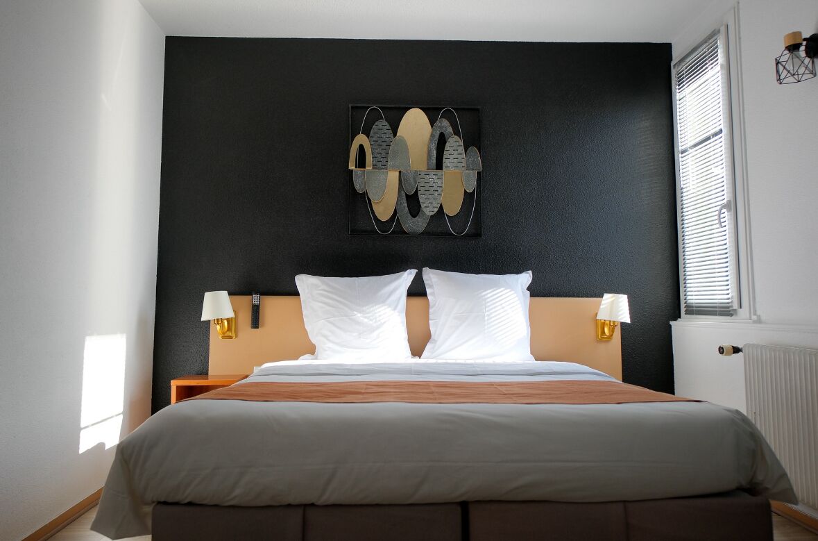Et moderne hotelværelse med en stor seng, to sengeborde med lamper, en væg i sort farve og et vindue med persienner.