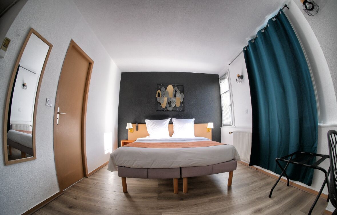 A bedroom with a bed, a nightstand, a chair, a mirror, and a window with curtains.