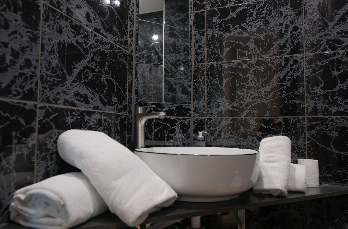A modern bathroom with a large sink, dark marble tiles, and white towels.