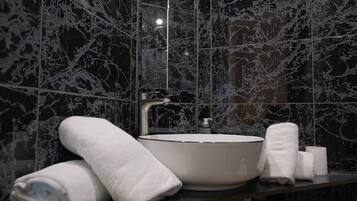 A modern bathroom with a large sink, dark marble tiles, and white towels.