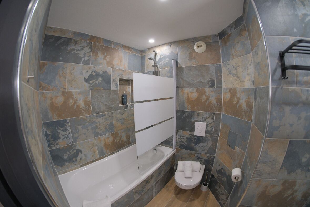 A bathroom with a bathtub, toilet, and shower area, featuring a unique tile pattern.