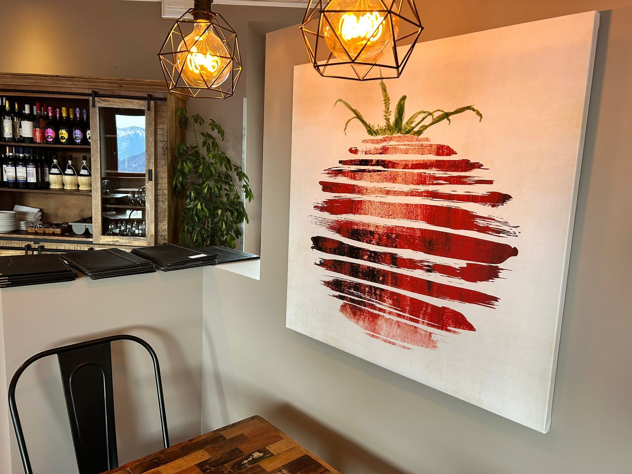 A restaurant interior with a bar area, a wooden table, and a large abstract painting on the wall.