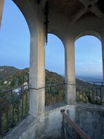 A balcony with a metal railing overlooking a scenic landscape with hills and a body of water.