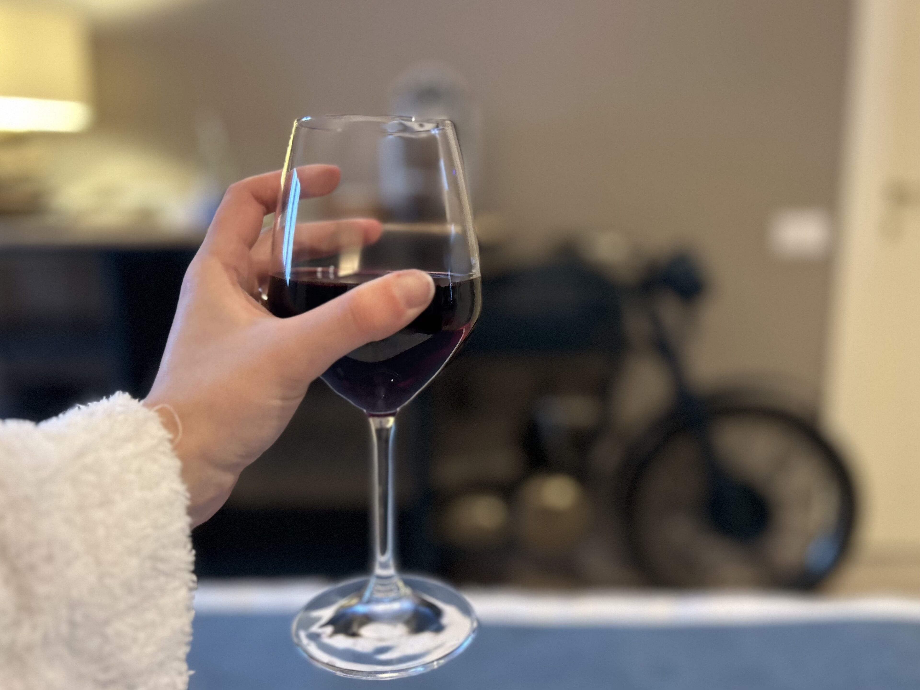 Une main tenant un verre de vin, avec un arrière-plan flou représentant une pièce.