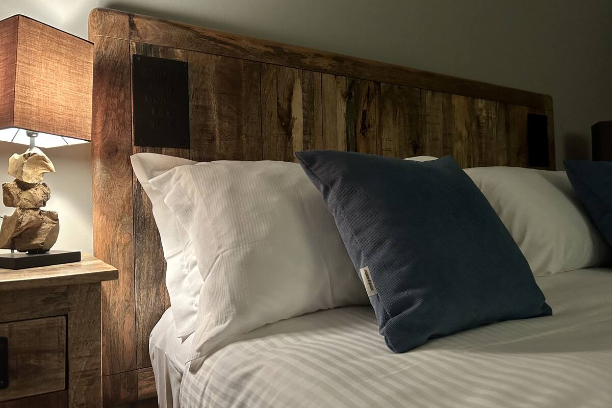 Een bed met witte en blauwe kussens, een houten hoofdbord en een nachtkastje met een lamp.