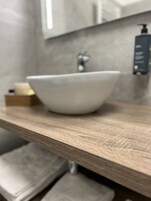 Un baño con tocador de madera, lavamanos blanco y dispensador de jabón.