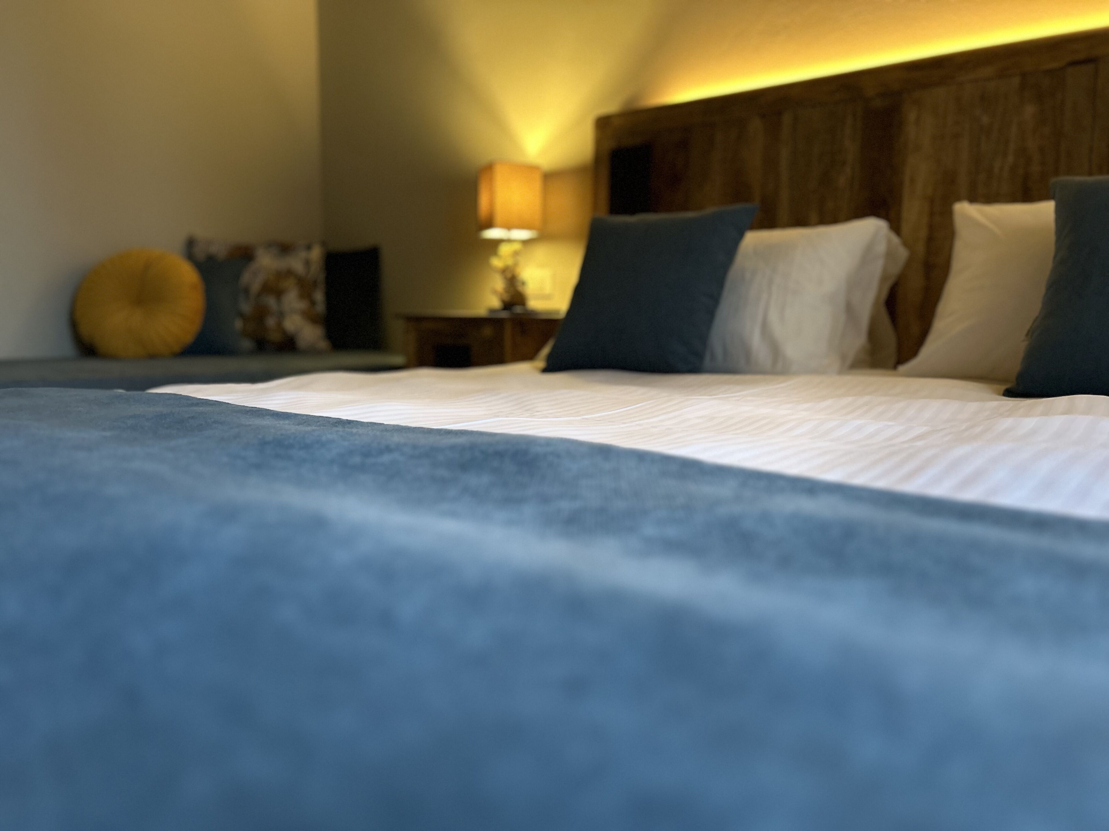 Un lit bien fait, avec une couverture bleue, une tête de lit en bois et une lampe de chevet.