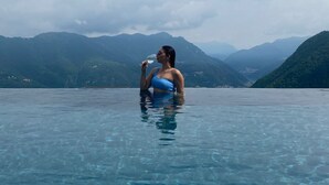 Una persona en traje de baño azul en una piscina cristalina, con un paisaje montañoso al fondo.