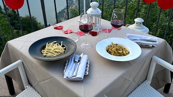 A table set for two with pasta dishes, wine glasses, and a candle, overlooking a mountainous landscape.