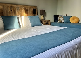 Una cama con cabecera de madera, una mesita de noche con lámpara y un sofá azul con cojines estampados.