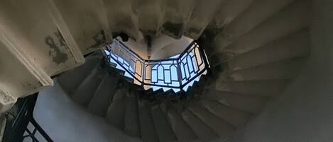 A spiral staircase with a metal railing and a view of the sky through a window at the top.