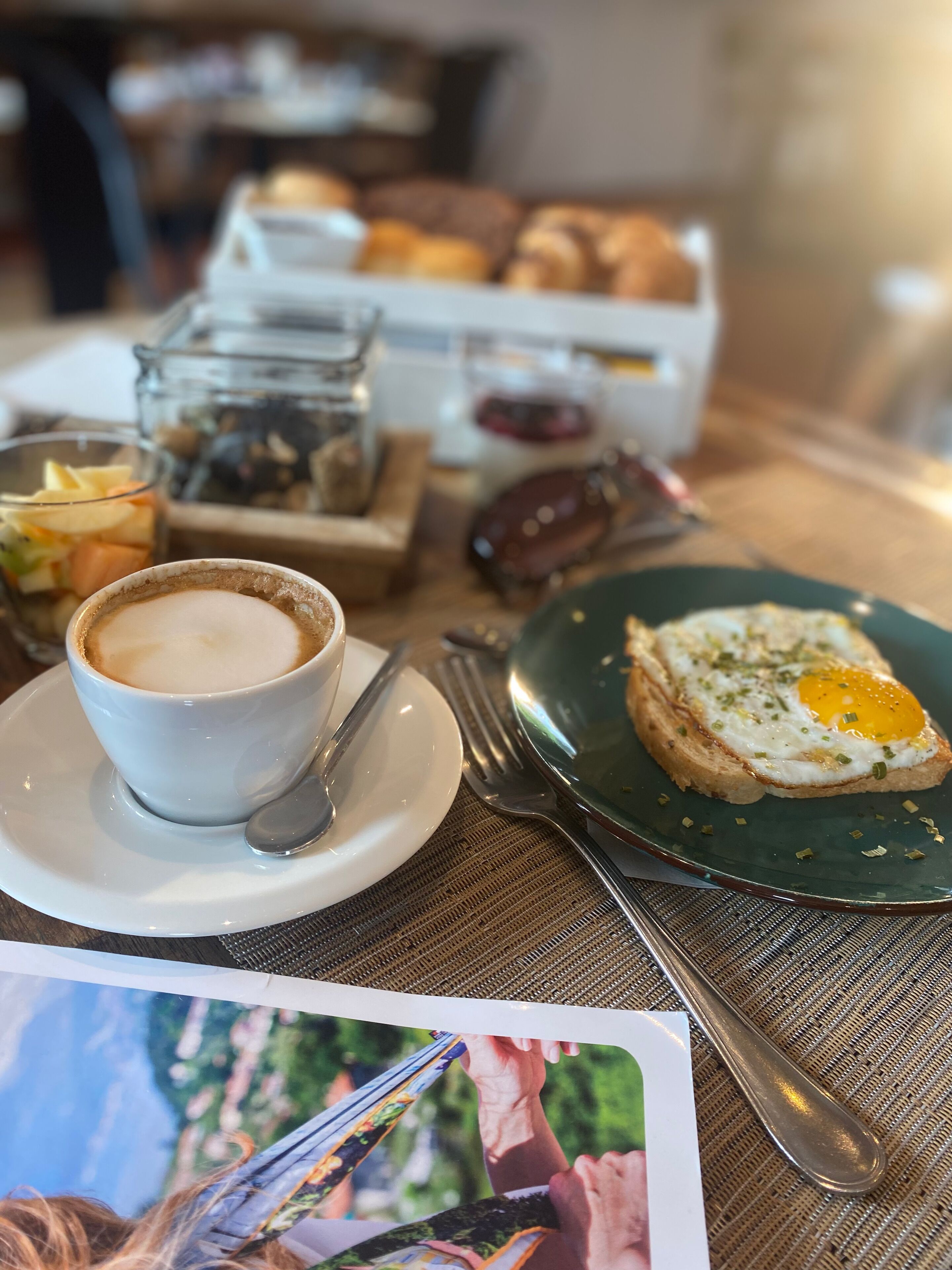 Un desayuno con una taza de café, tostadas con huevo y un vaso pequeño de jugo sobre una mesa.