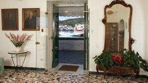 A hotel lobby with a tiled floor, a wooden bench with flowers, a large mirror, and two framed portraits on the wall.