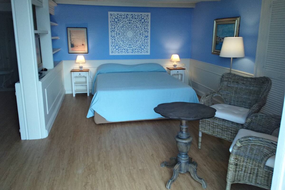 Un dormitorio con una cama, dos mesitas de noche con lámparas, una silla y un adorno en la pared.
